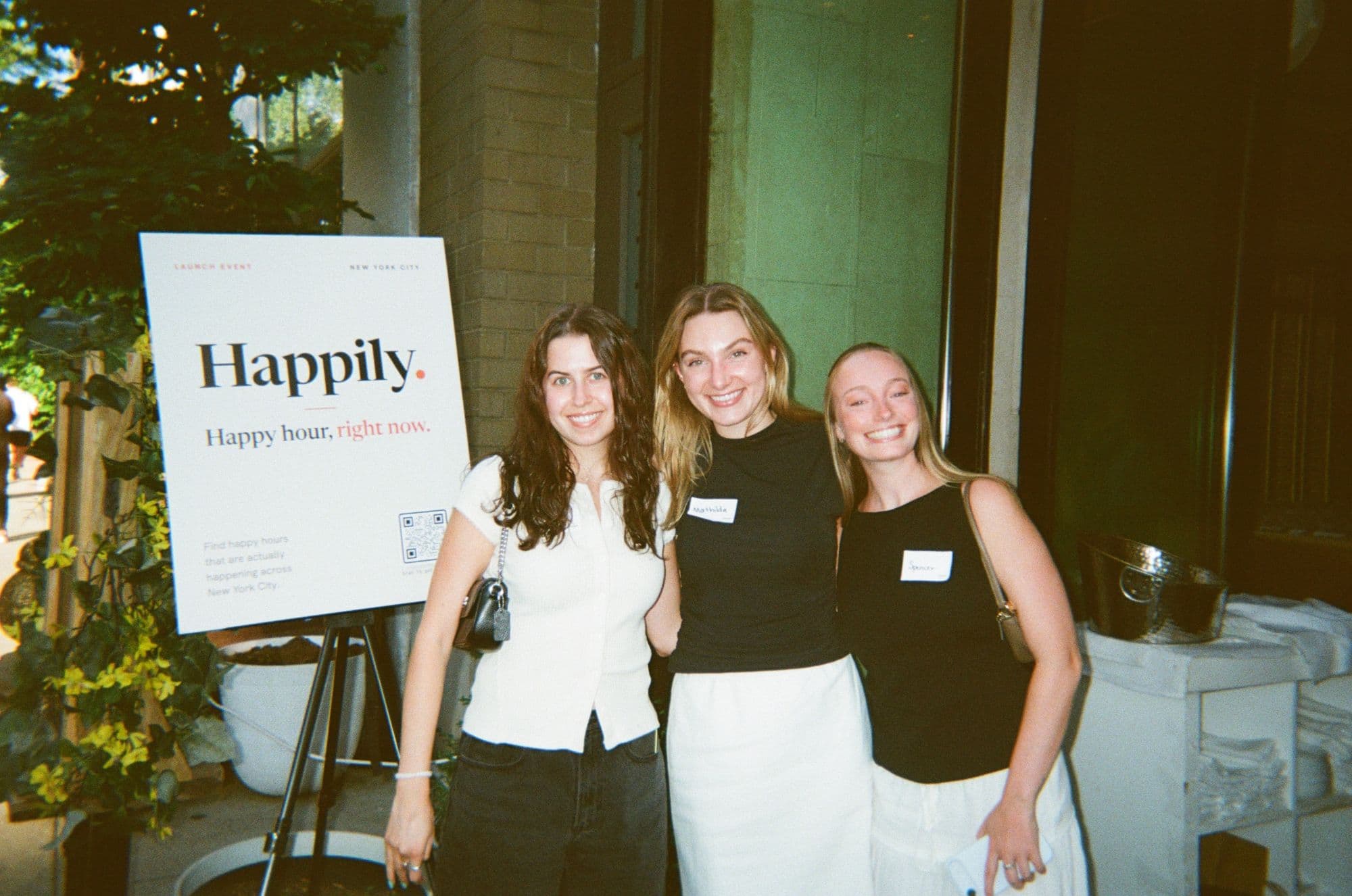 Three guests smiling next to the Happily sign at the launch event