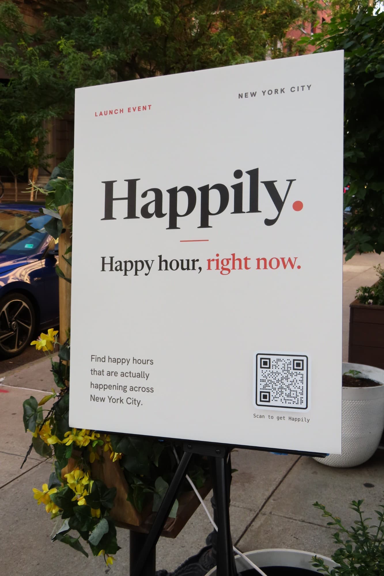 Happily launch event sign on an easel outside a West Village restaurant